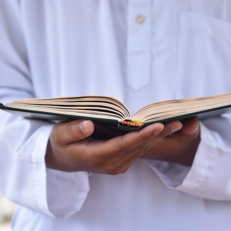 Holy Quran in hand with arabic calligraphy meaning of Al Quran. Islamic concept background